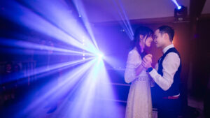Couple échangeant une danse intime sous les lumières colorées et effets lumineux en fin de soirée de mariage.