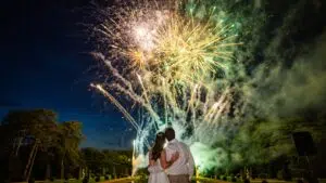 Un couple, bras dessus bras dessous, admire un feu d'artifice aux couleurs chatoyantes qui illumine le ciel nocturne au-dessus du jardin du château de Breteuil.