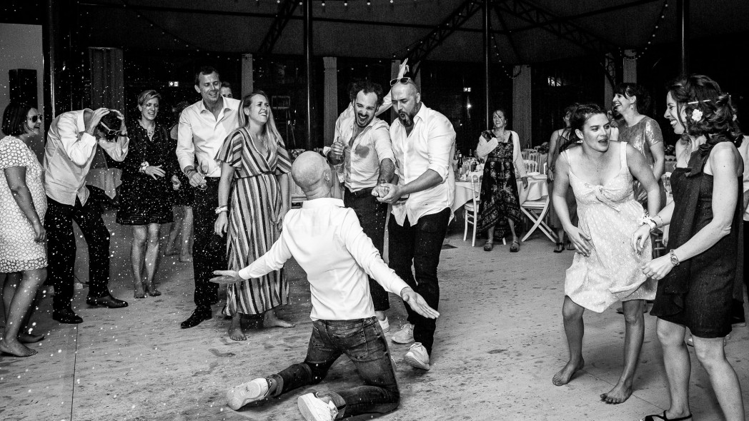 un homme à genou aspergé de champagne avec les gens autour qui rigolent